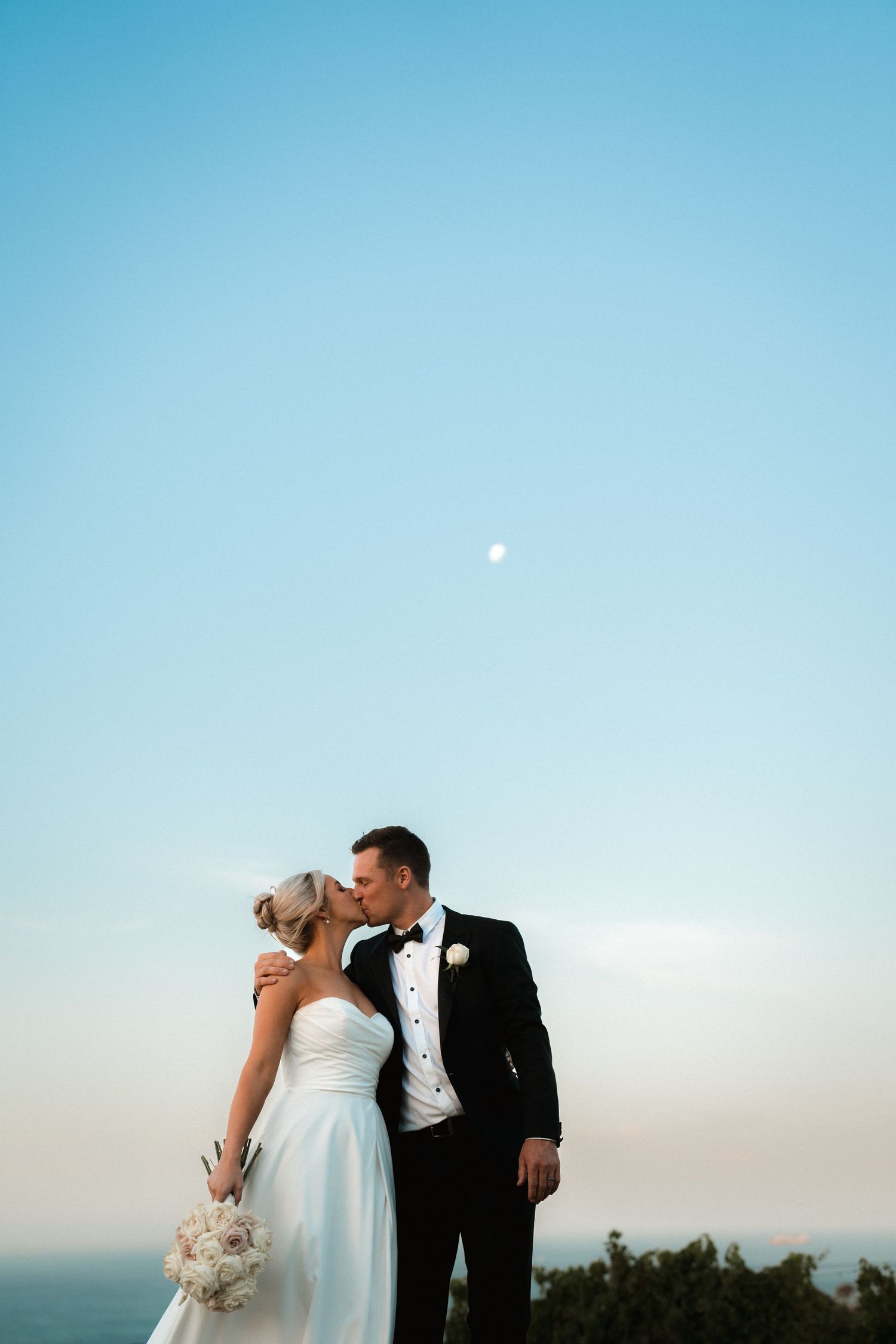 Romantic coastal wedding portrait with a full moon in the blue sky.