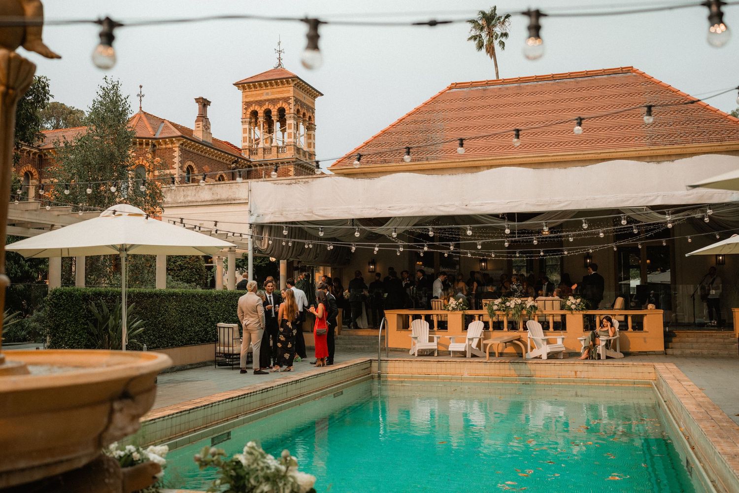 An elegant outdoor wedding venue with string lights and a swimming pool surrounded by Spanish-style architecture.