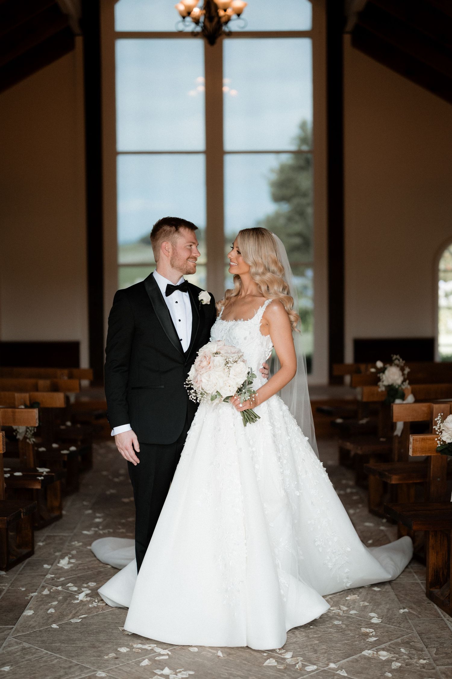 Classic wedding portrait in a church with stained glass windows and wooden pews.