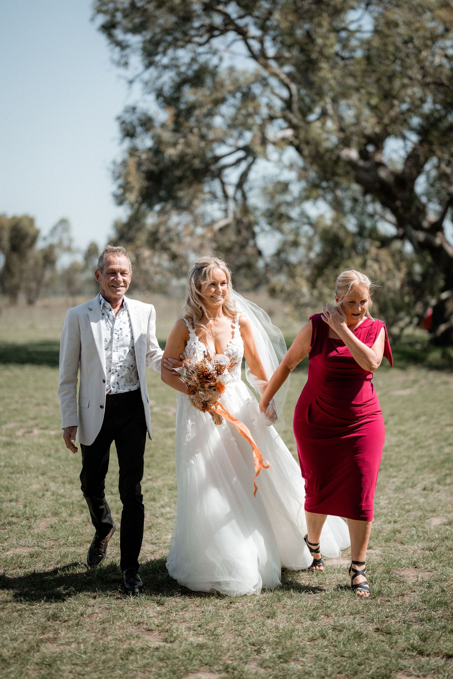 Wedding party walks together across sunny outdoor field.