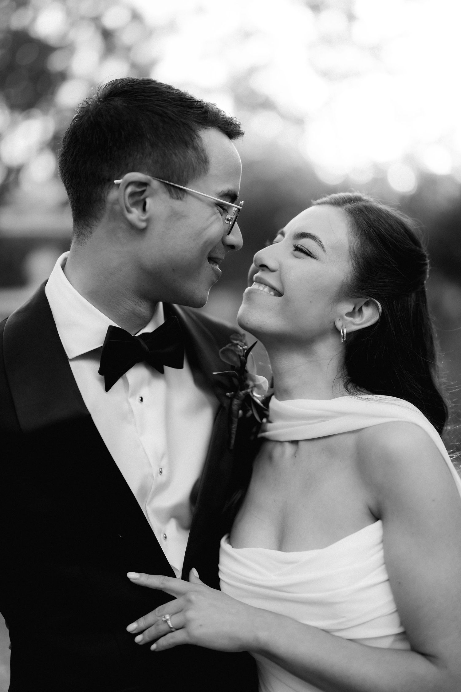 Joyful bride and groom share an intimate moment laughing together in a classic black and white wedding portrait.