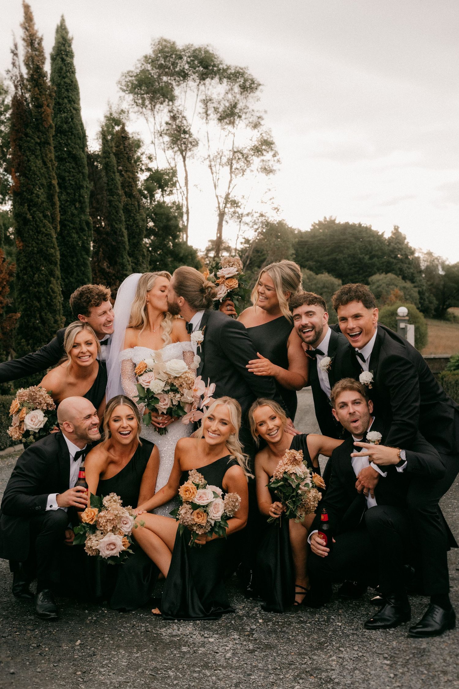 Wedding party poses playfully in a line on the ground during golden hour for candid group photos.