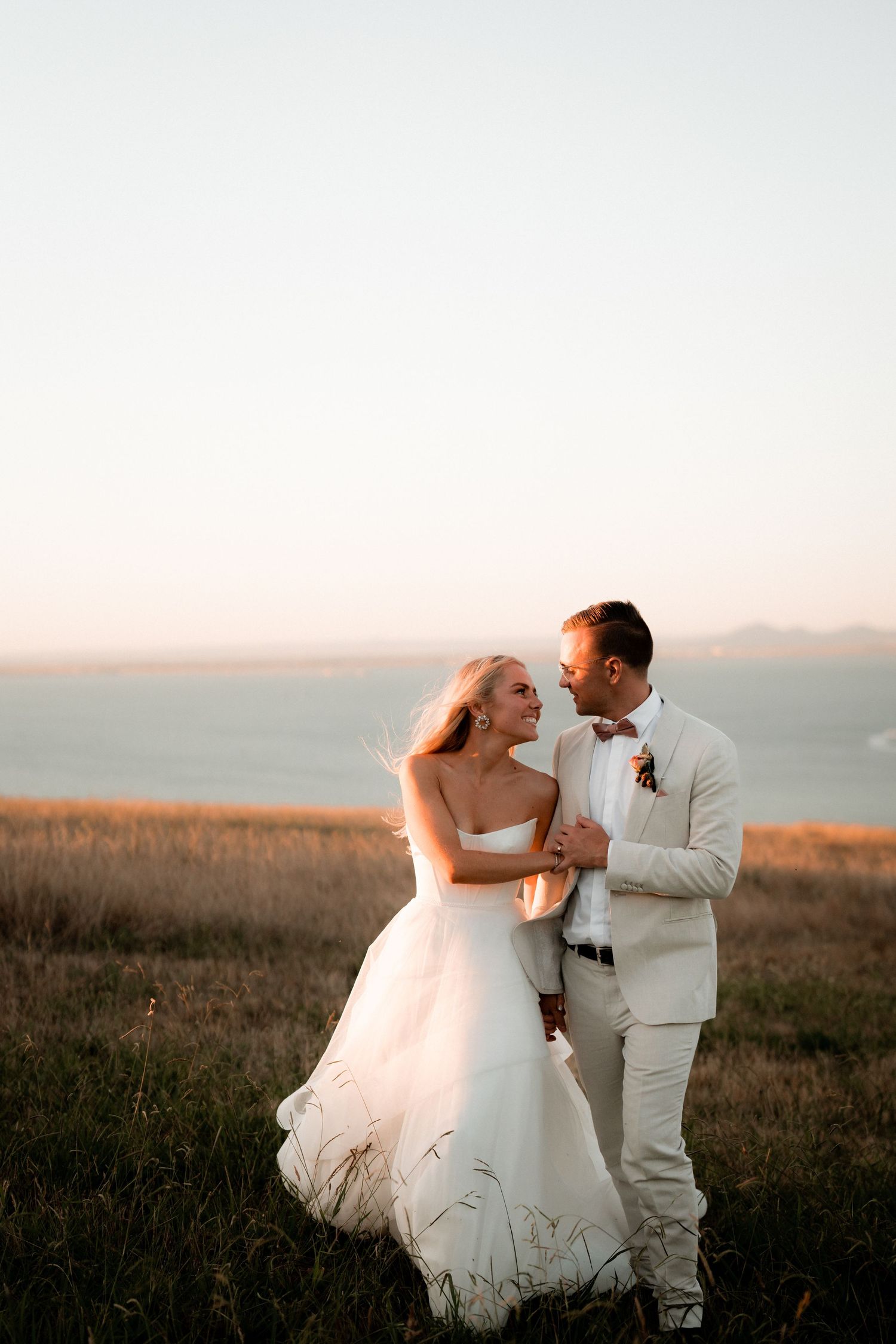 Newlyweds share an intimate moment in a field during golden hour.