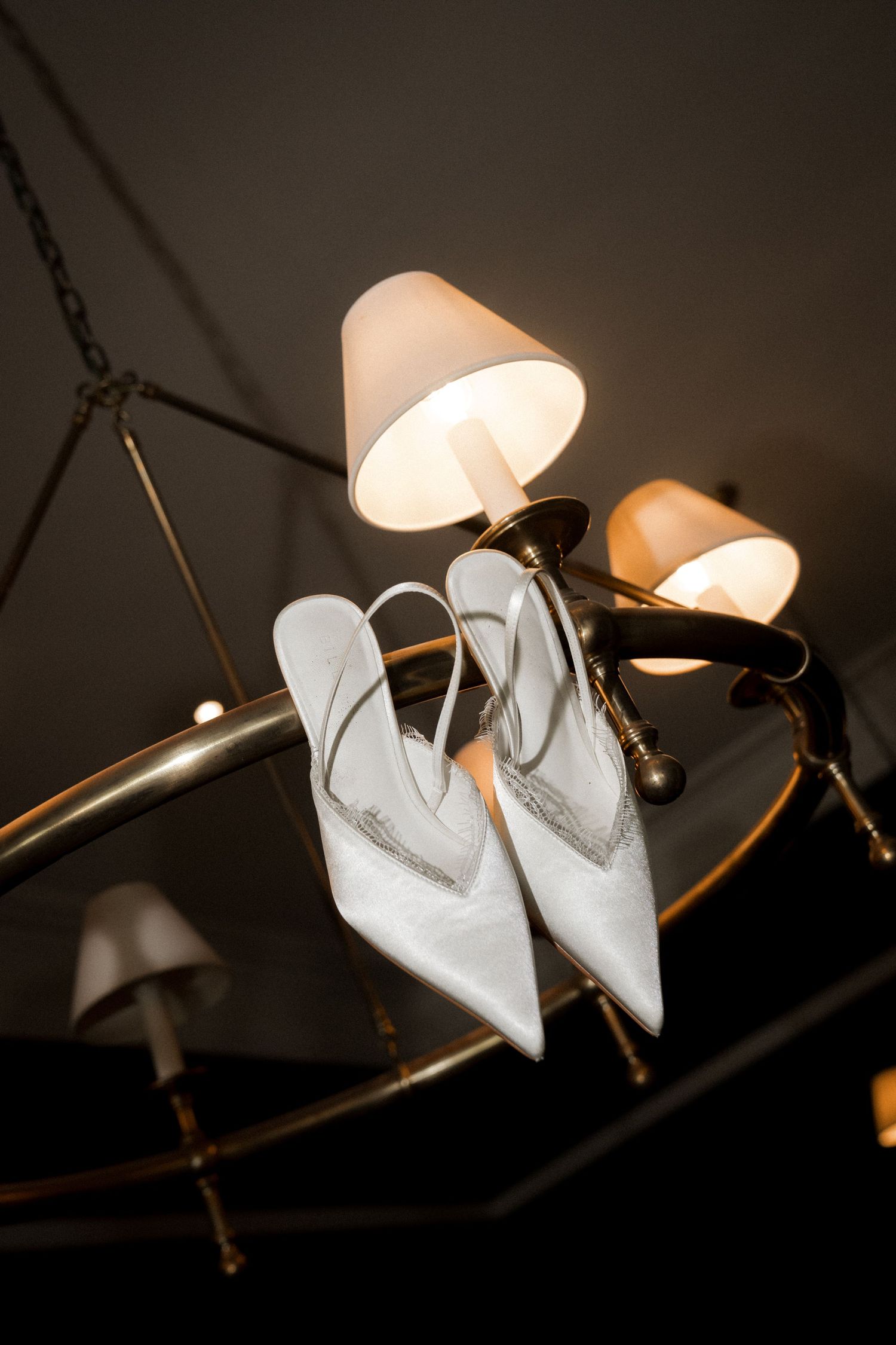 Elegant white bridal shoes displayed on a decorative light fixture against a dark background.