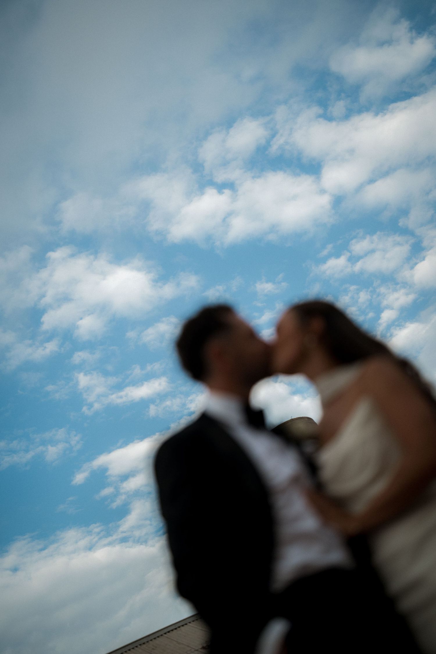 Silhouetted couple embracing against a bright blue sky with wispy white clouds.