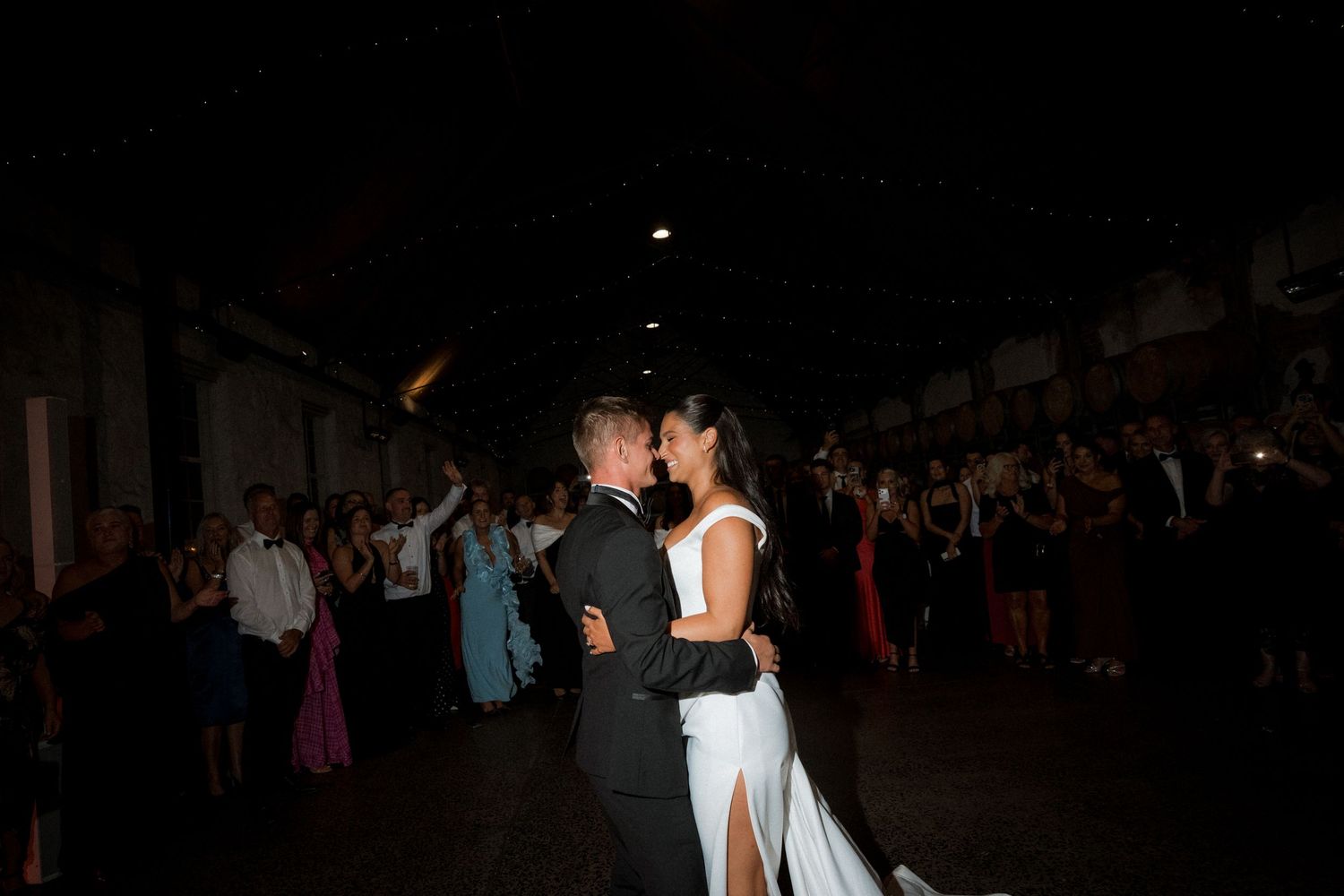 Dark silhouettes of wedding guests dancing on a dimly lit dance floor at night.
