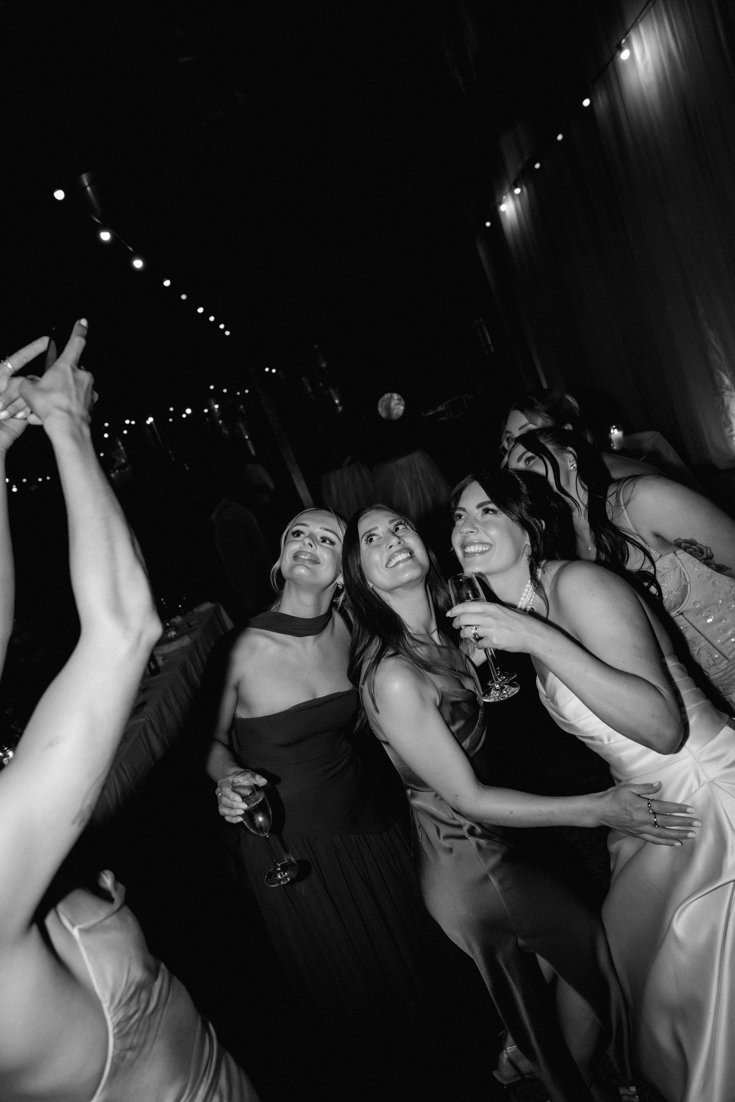Black and white photo of a crowded dance floor with people dancing with their hands raised at a party.