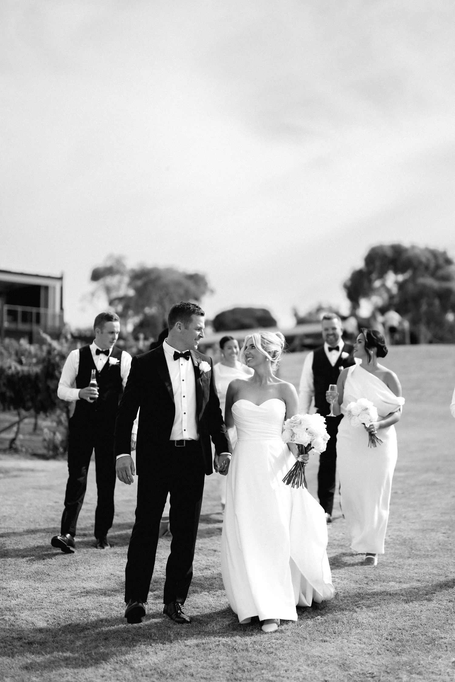 A wedding party walks together on a lawn in black and white formal attire.