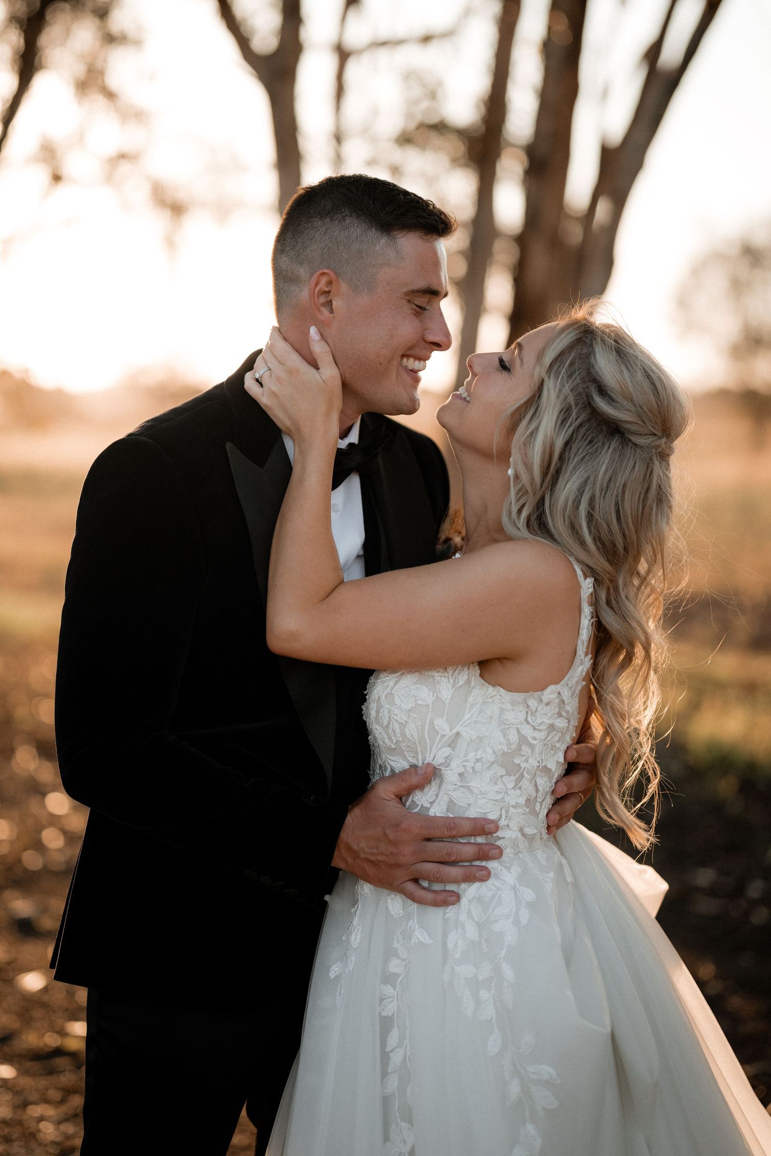 Romantic sunset portrait of couple embracing in formal wedding attire.