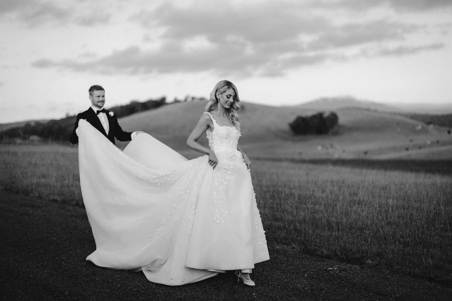 Dramatic black and white photo of couple with flowing wedding dress against rolling hills.