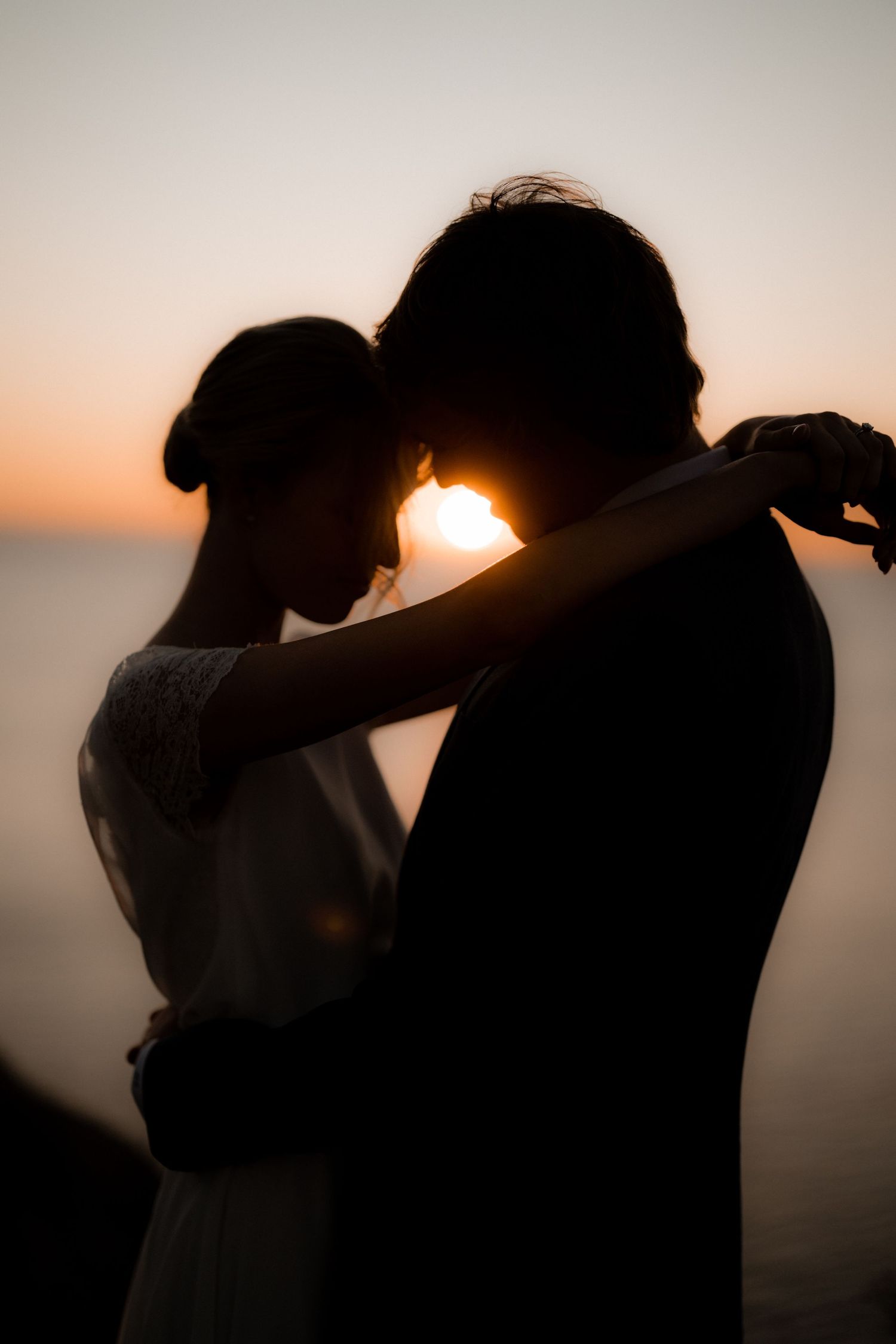 Silhouette of newlyweds embracing at sunset with golden light between them.