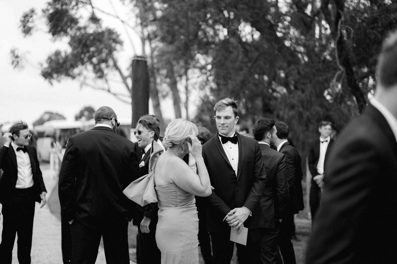 Guests mingle at an elegant black tie outdoor event in a monochrome black and white photograph.
