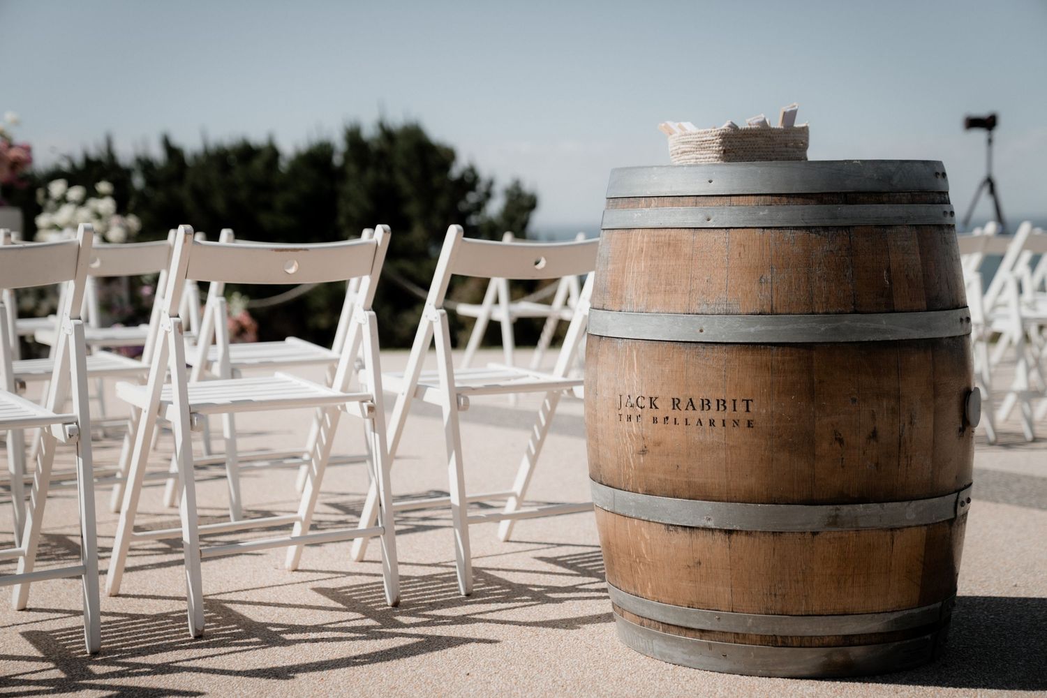 Rustic wooden barrels and white chairs set up for an outdoor wedding ceremony.