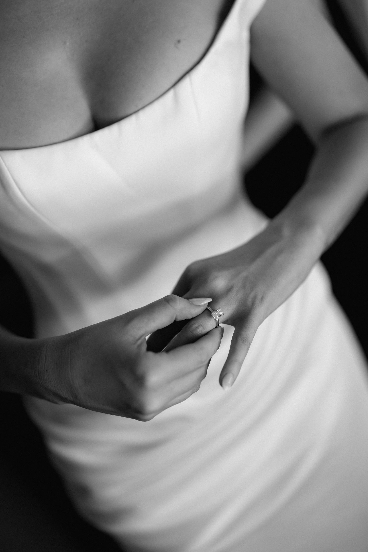 Close-up black and white detail of hands adjusting a wedding ring on white dress.