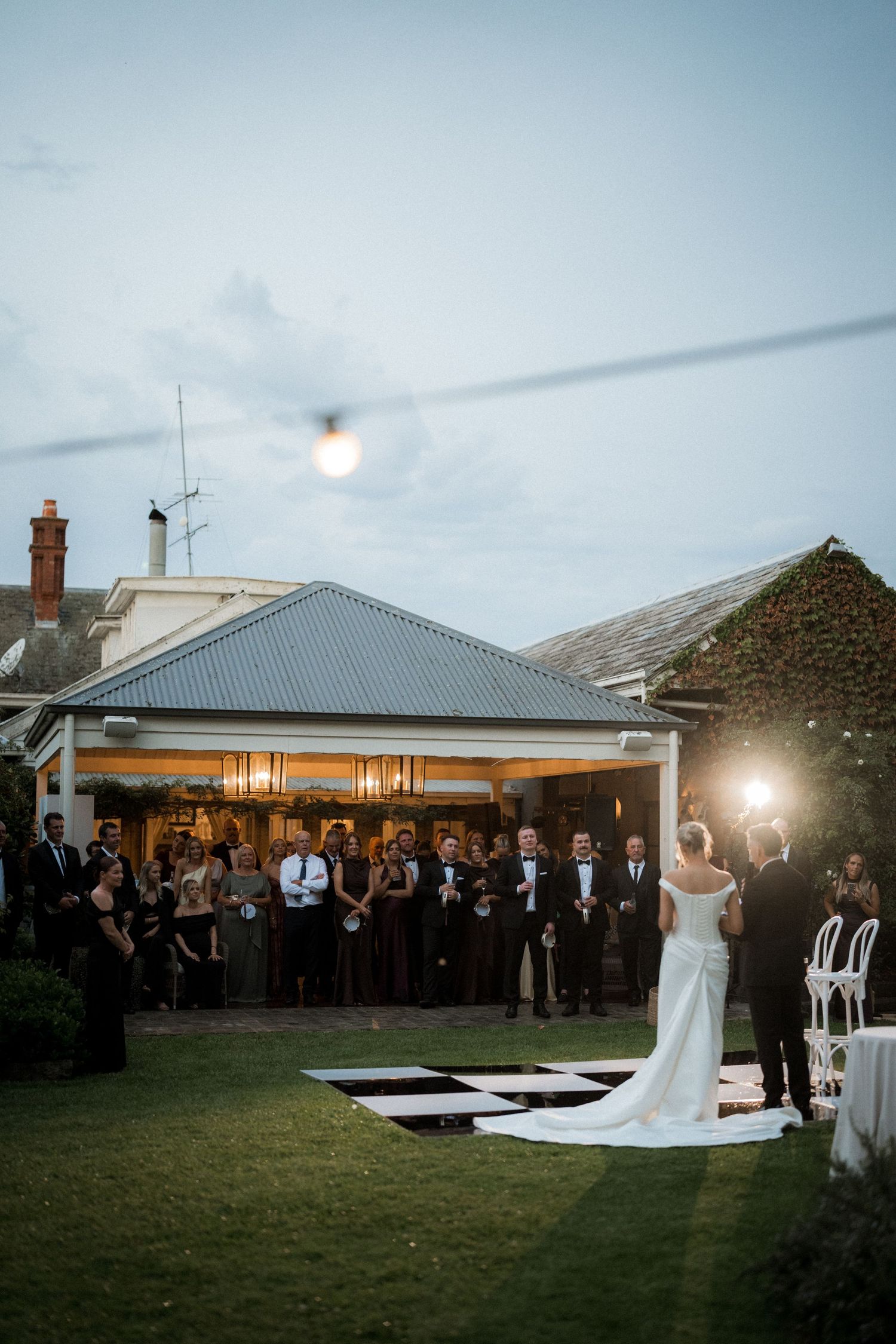 Evening wedding reception setup with white dance floor and string lights outdoors.