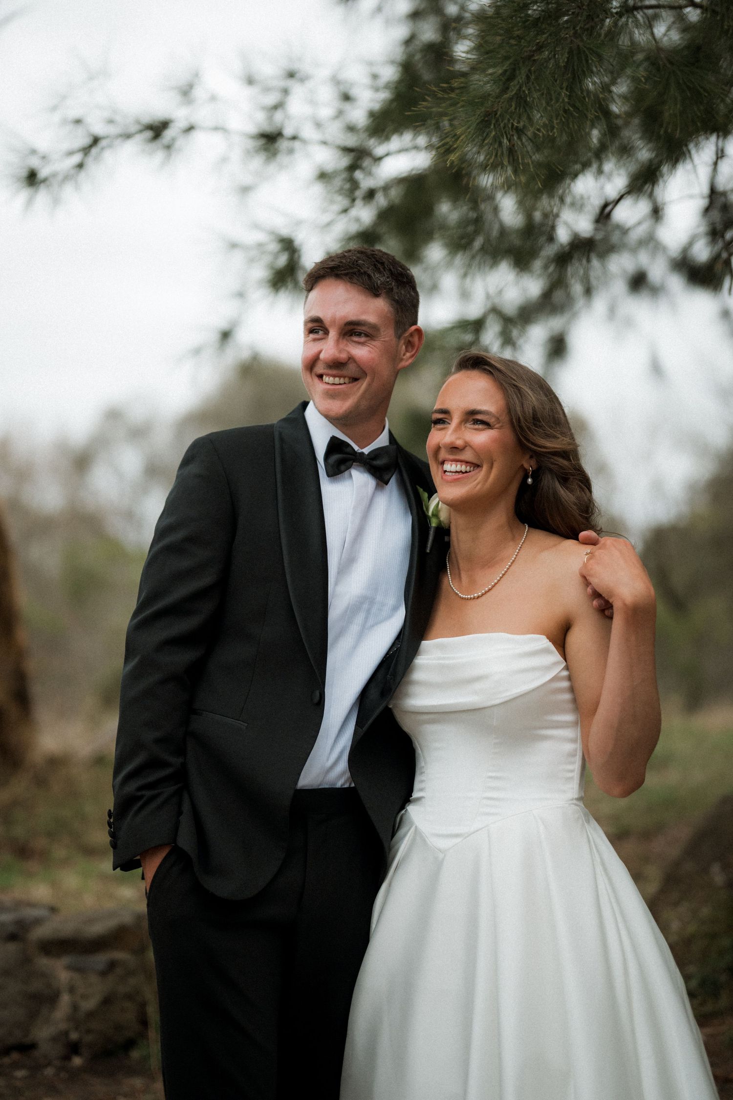 A joyful wedding couple shares an intimate moment outdoors with natural greenery in the background.