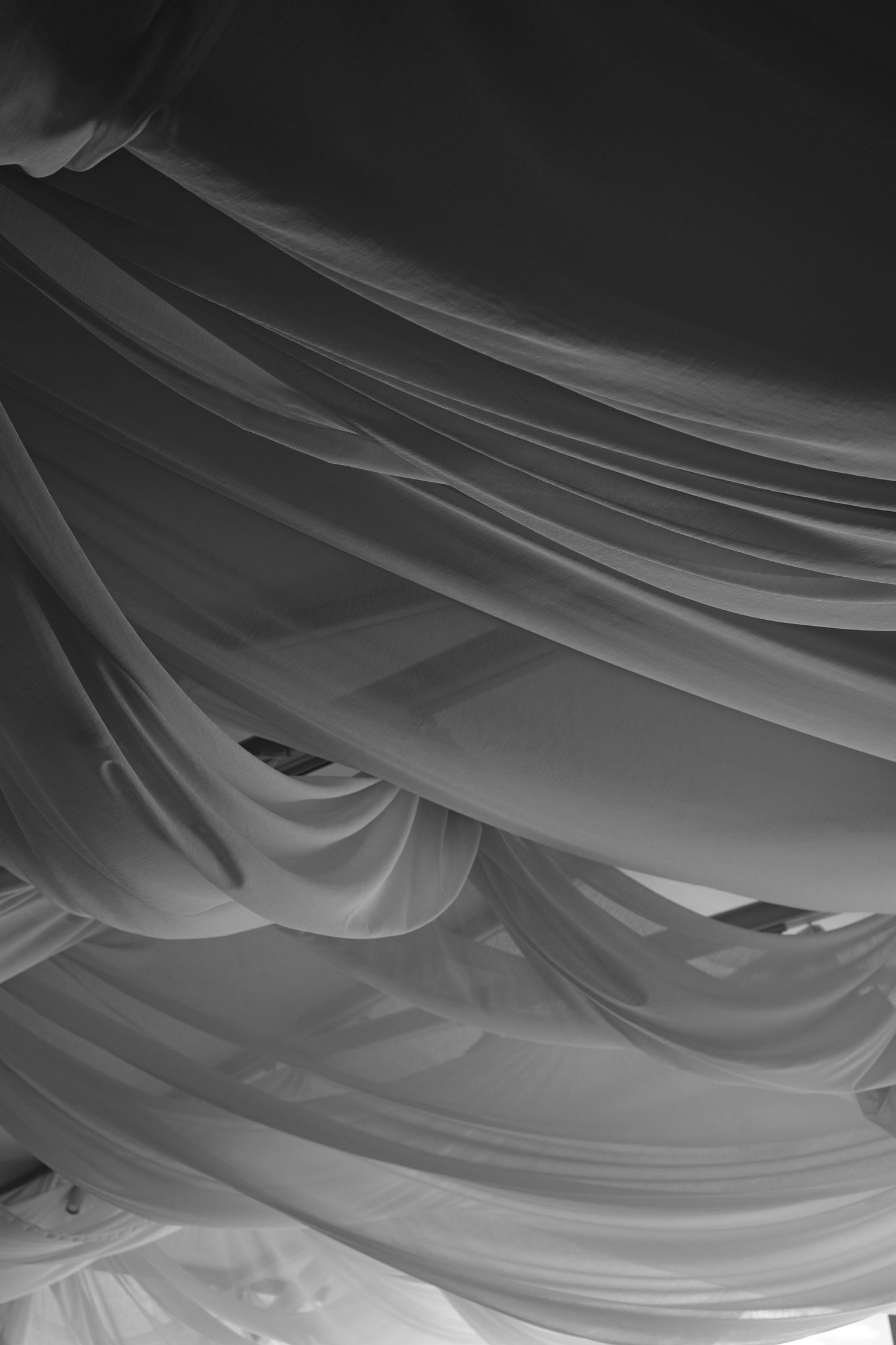 A black and white photo of soft, flowing sheer fabric draped in layers from a ceiling, creating an elegant wedding decor effect.