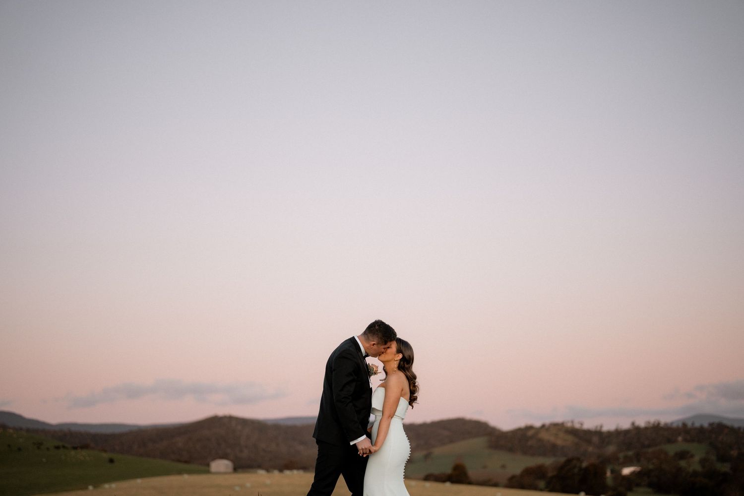 Silhouettes of couple embracing against sunset sky with mountains in background.