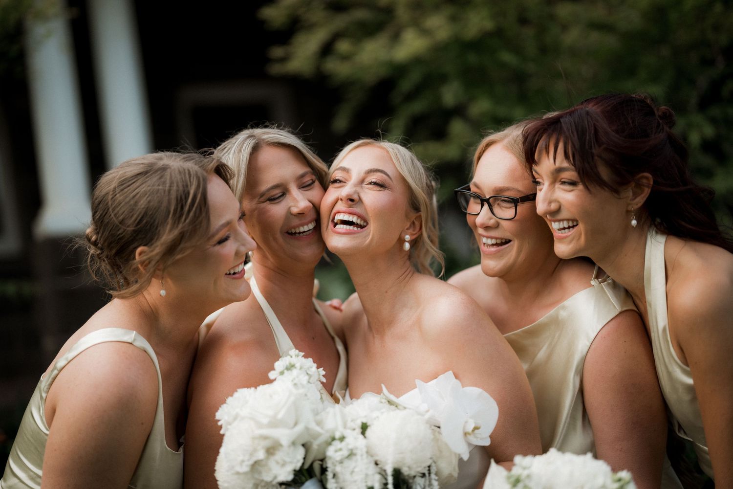 Bridesmaids in white dresses sharing laughter and embracing during wedding celebrations.