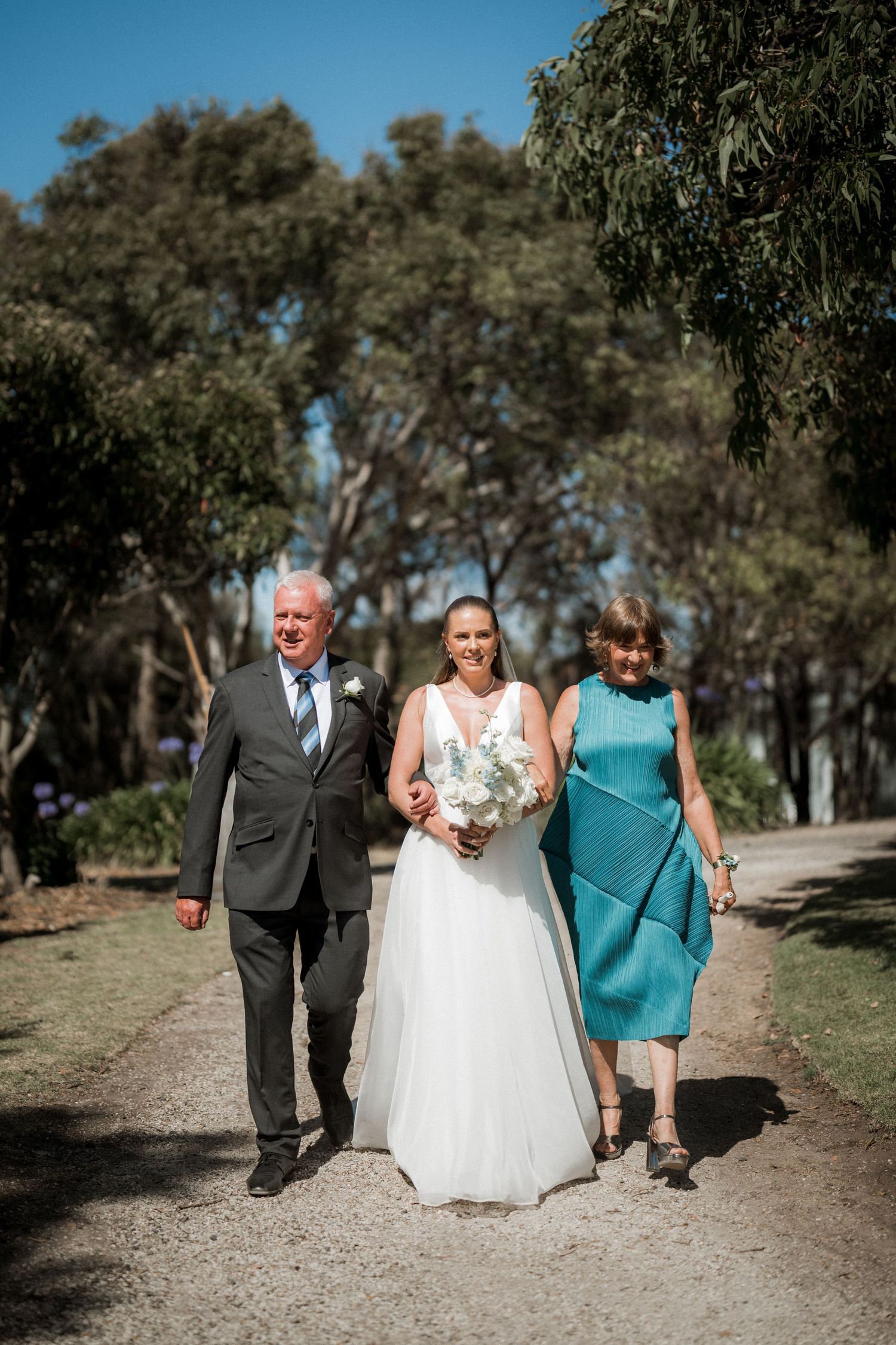 Wedding party walking down a tree-lined path on a sunny day.