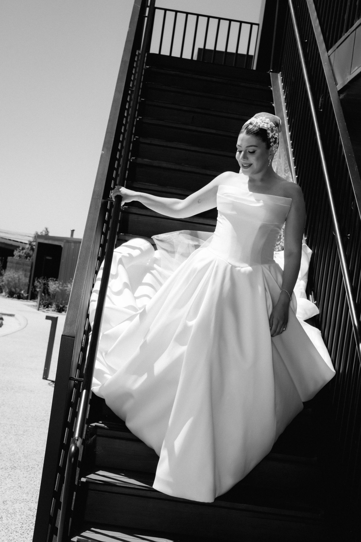 Flowing white wedding dress captured in artistic black and white shots on stairs.