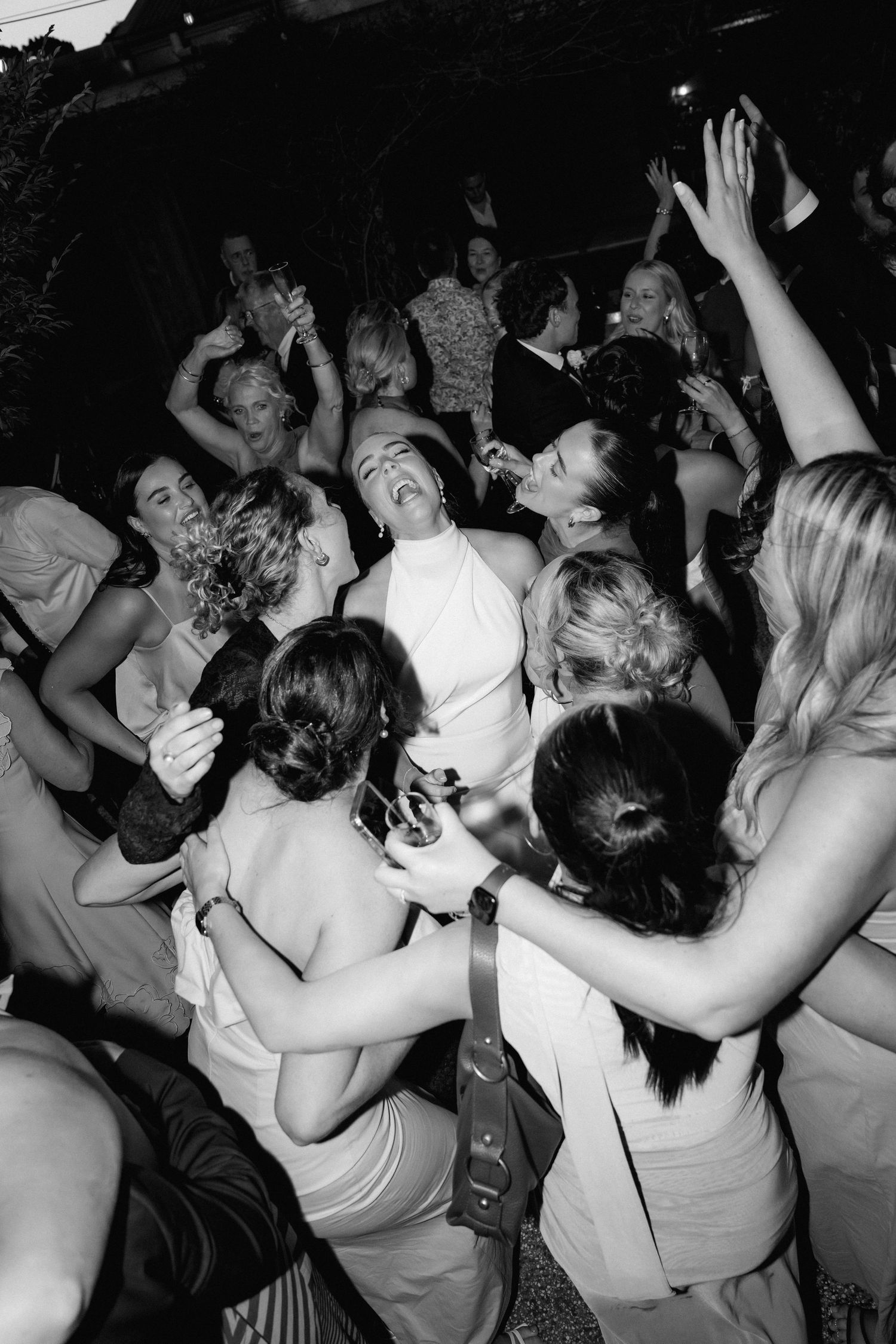 A lively crowd of wedding guests dancing and celebrating on a dark dance floor.