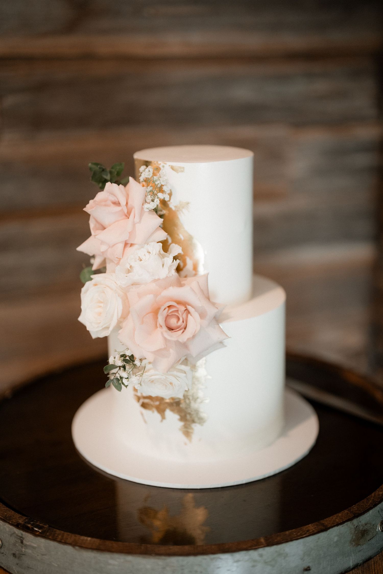 Elegant two-tier white wedding cake adorned with delicate pink roses and gold accents.