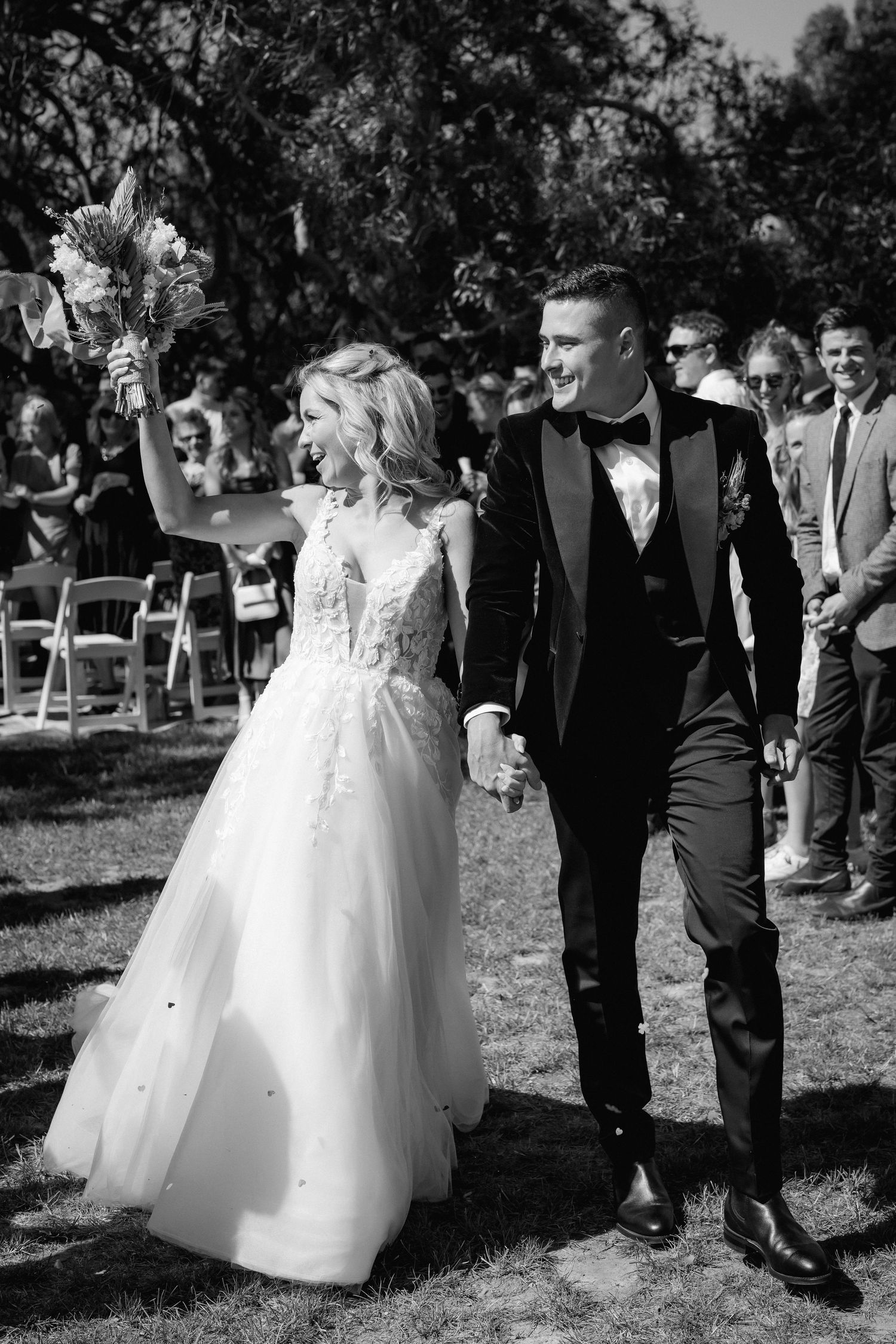 Elegant wedding couple walks together during recessional on grassy outdoor ceremony aisle.