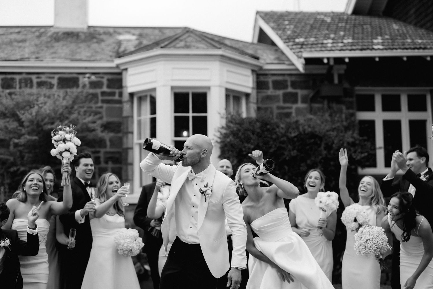 Black and white photo of joyful dancing at a wedding celebration outside a stone building.