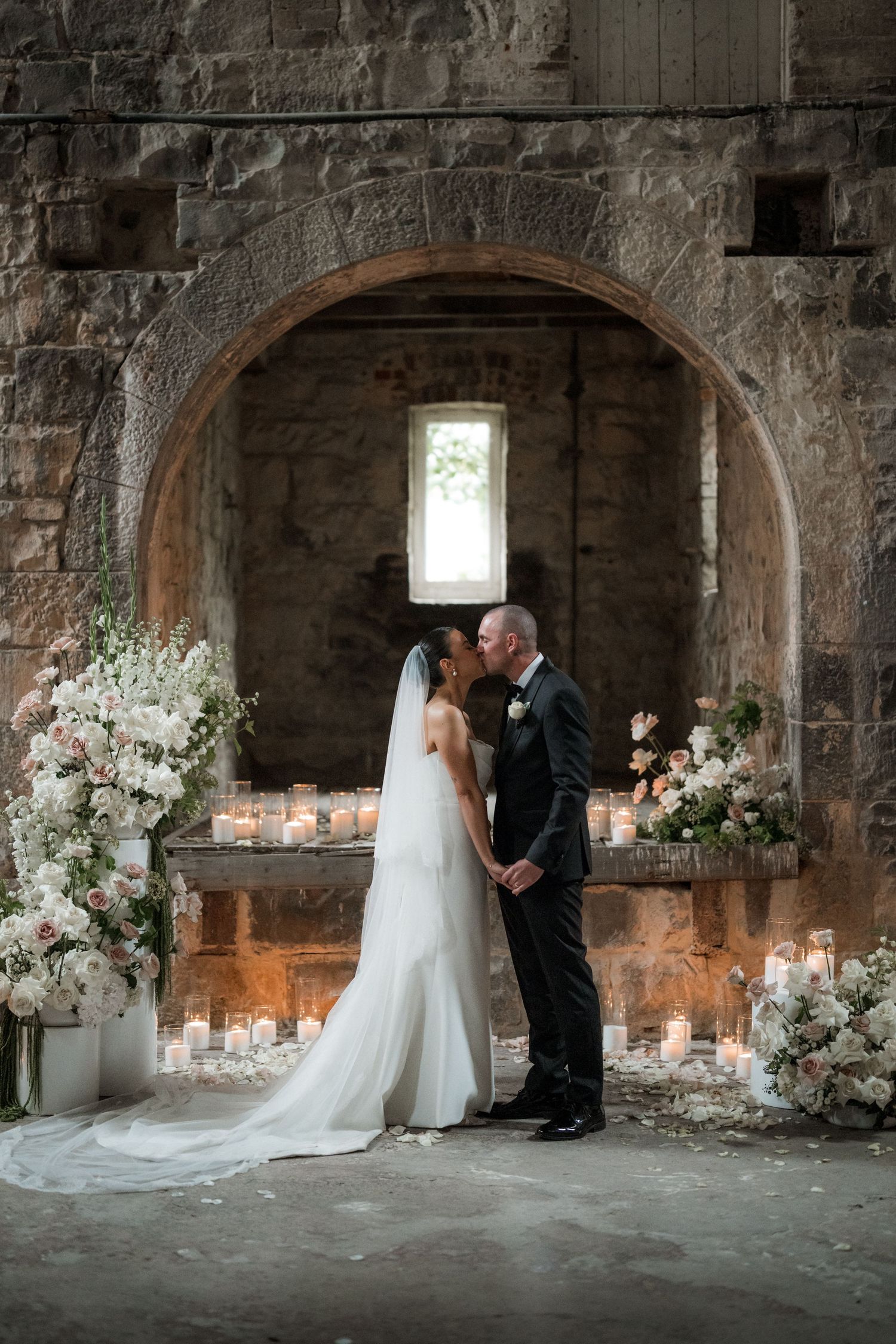 A romantic wedding ceremony setup in a stone archway decorated with candles and white flowers.
