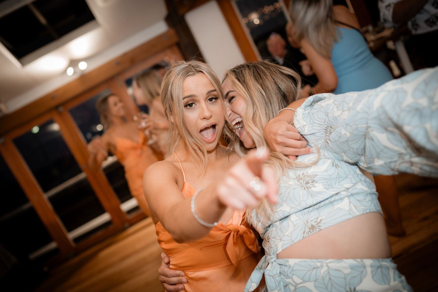 Two friends dancing and laughing together at a celebration in an indoor venue.