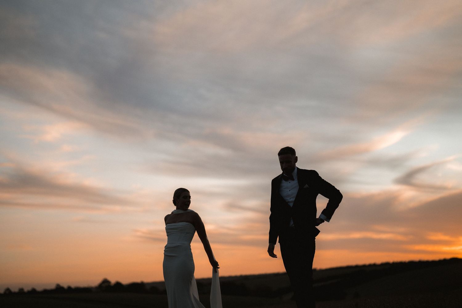 Silhouettes of wedding couple against dramatic sunset sky.