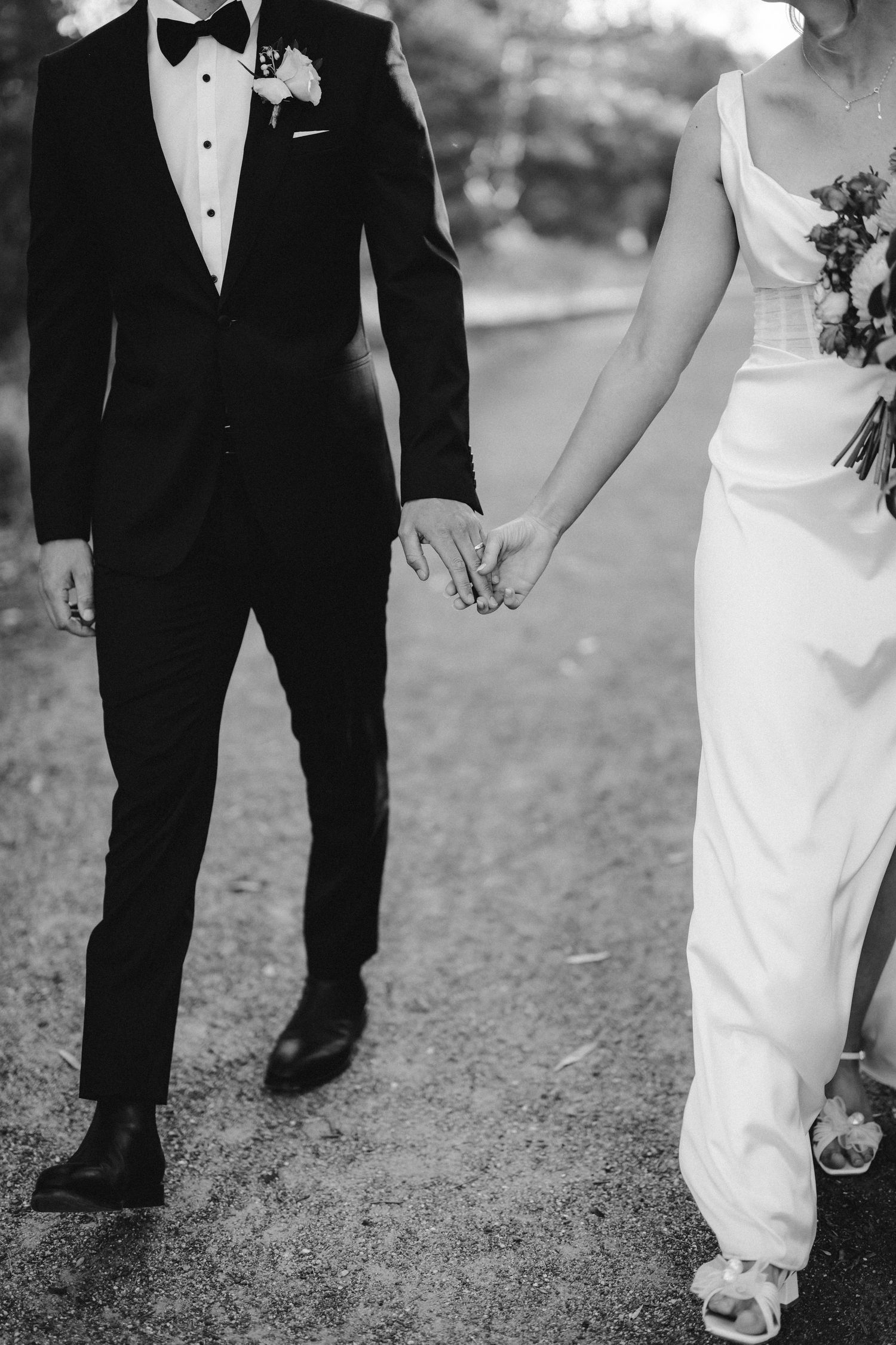Close up of newlywed couple holding hands while walking, showing elegant wedding attire in black and white.
