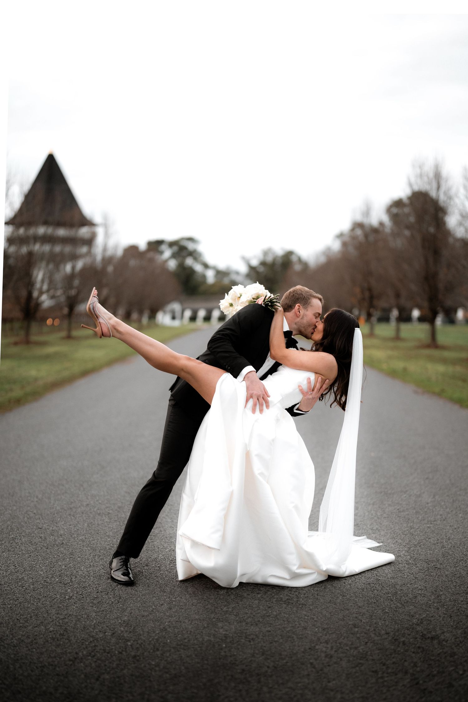 Romantic dip pose on pathway with historic building visible in background.