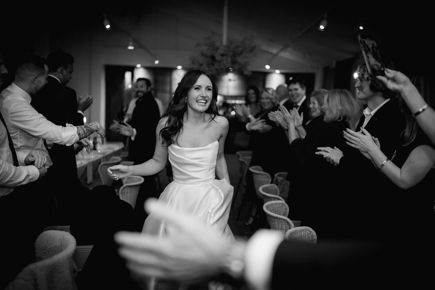 A black and white photo of a dance celebration at a wedding reception with people dancing and raising their hands.