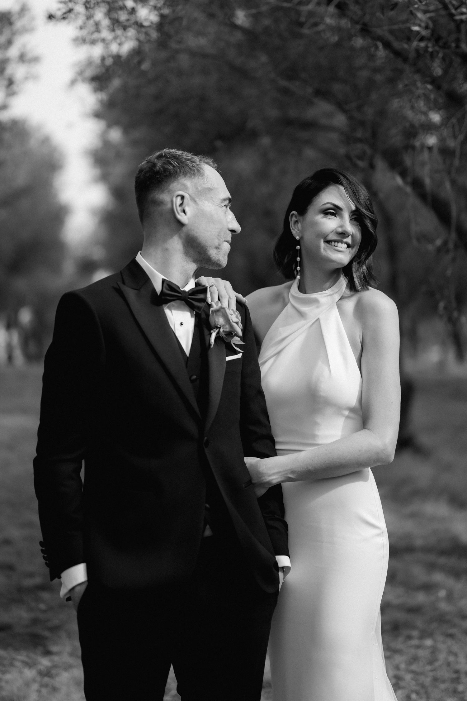 Elegant couple shares romantic moment in formal black and white attire during outdoor wedding photoshoot.