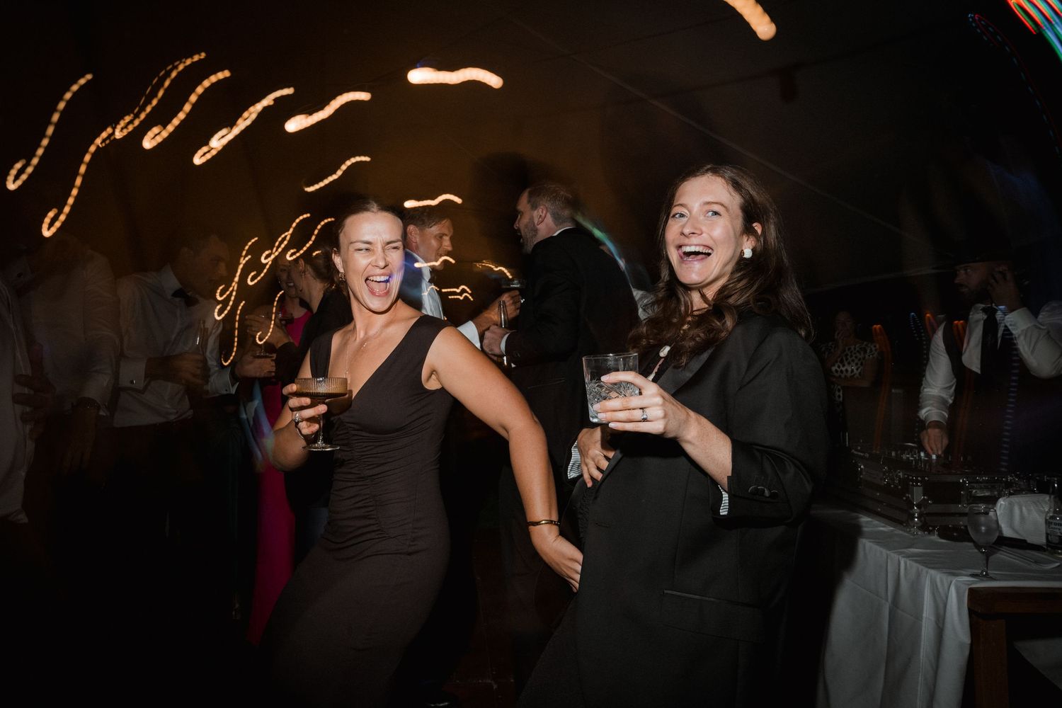 Wedding guests dancing and laughing at nighttime reception with string lights.