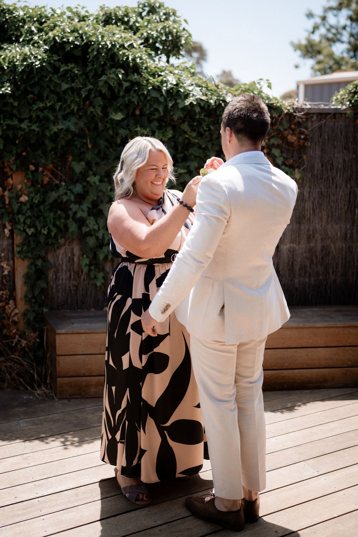 Couple sharing intimate moment on wooden deck surrounded by greenery during outdoor photoshoot.