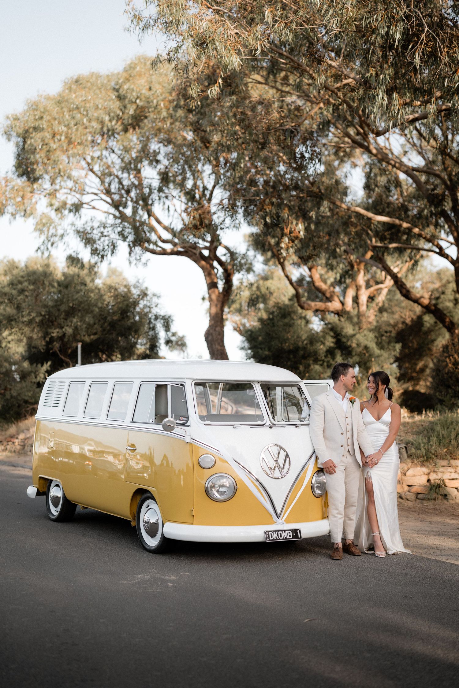 Classic yellow and white VW kombi van parked on a rural road for wedding photos.