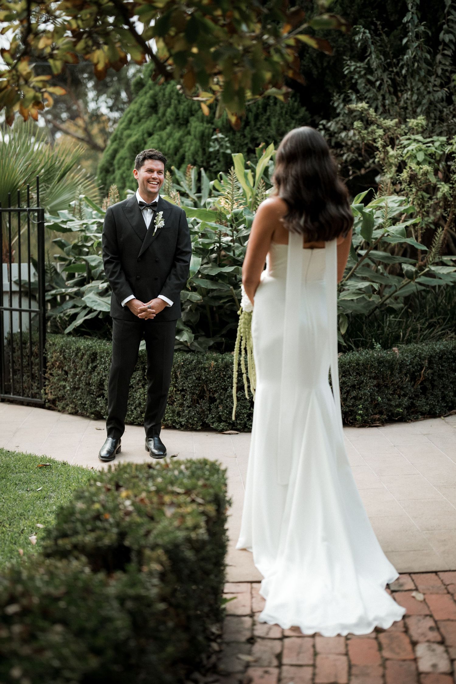 Wedding ceremony on a brick path surrounded by manicured garden hedges and greenery.