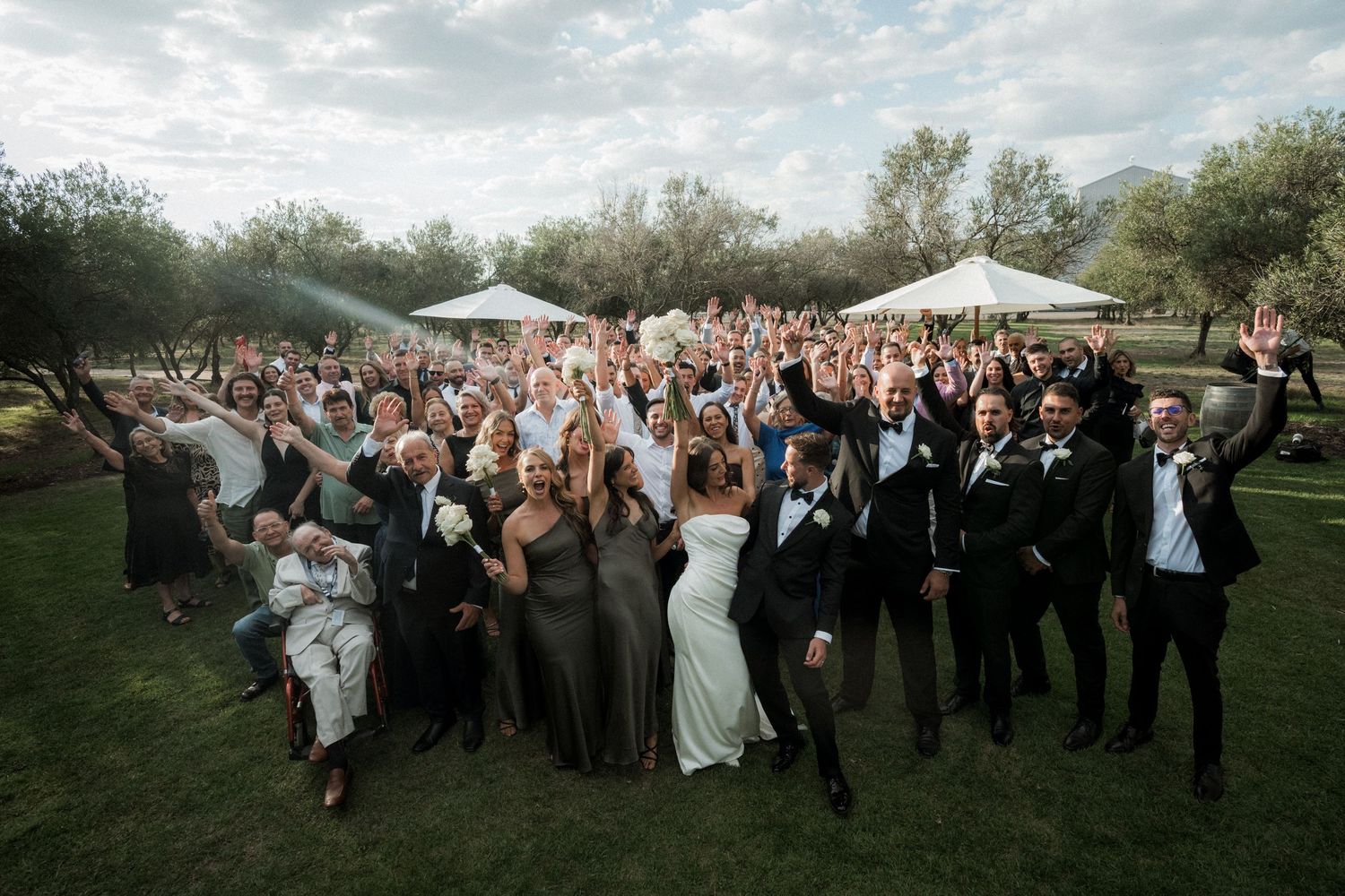 Wedding party members joyfully running and jumping together on a grassy lawn during an outdoor celebration.