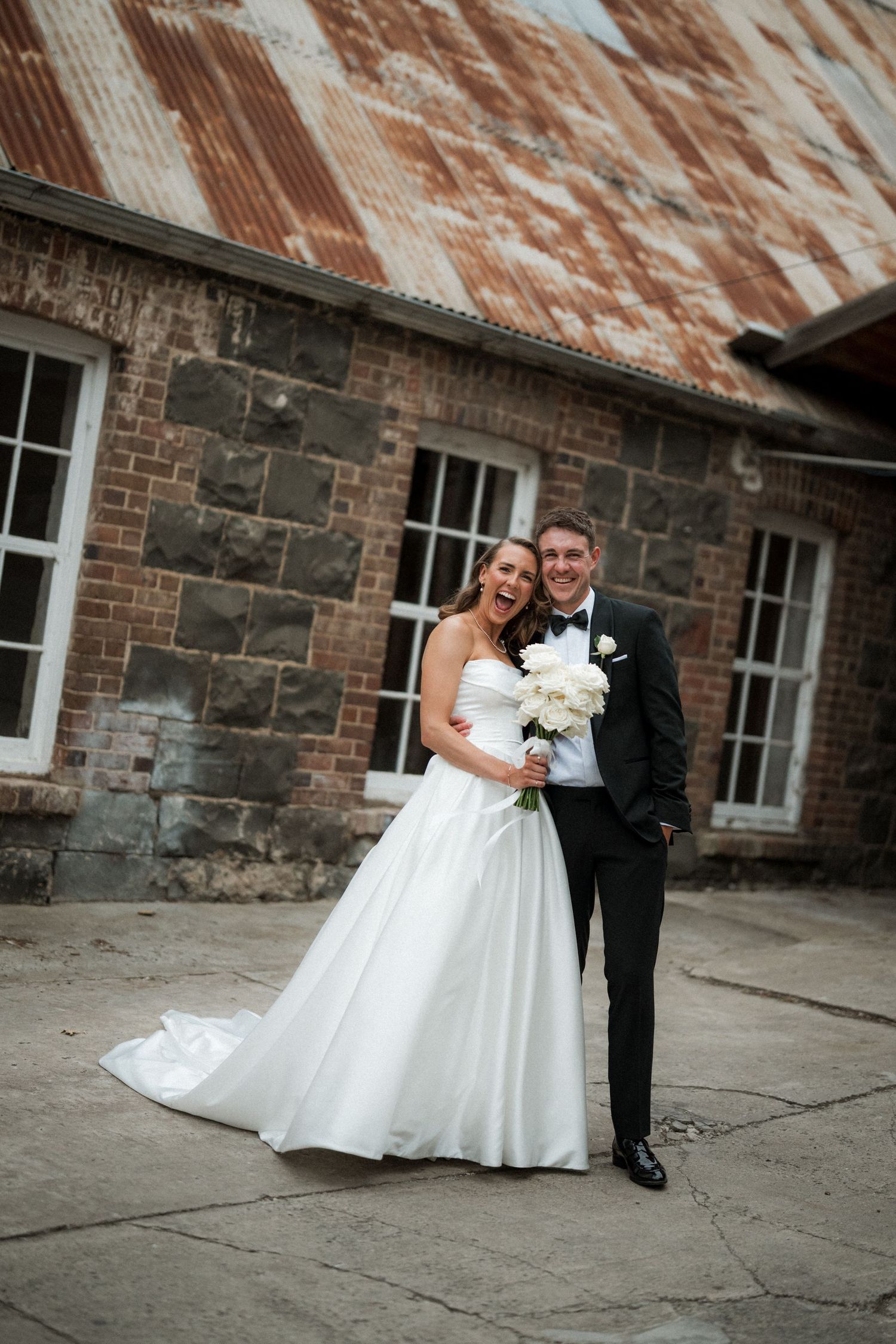 A wedding couple poses against a rustic stone and brick wall with peeling paint during their photo session.