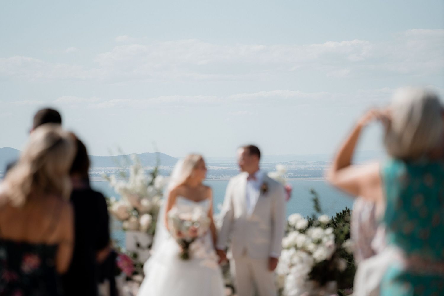 Wedding guests celebrate during an outdoor ceremony with confetti and raised arms.