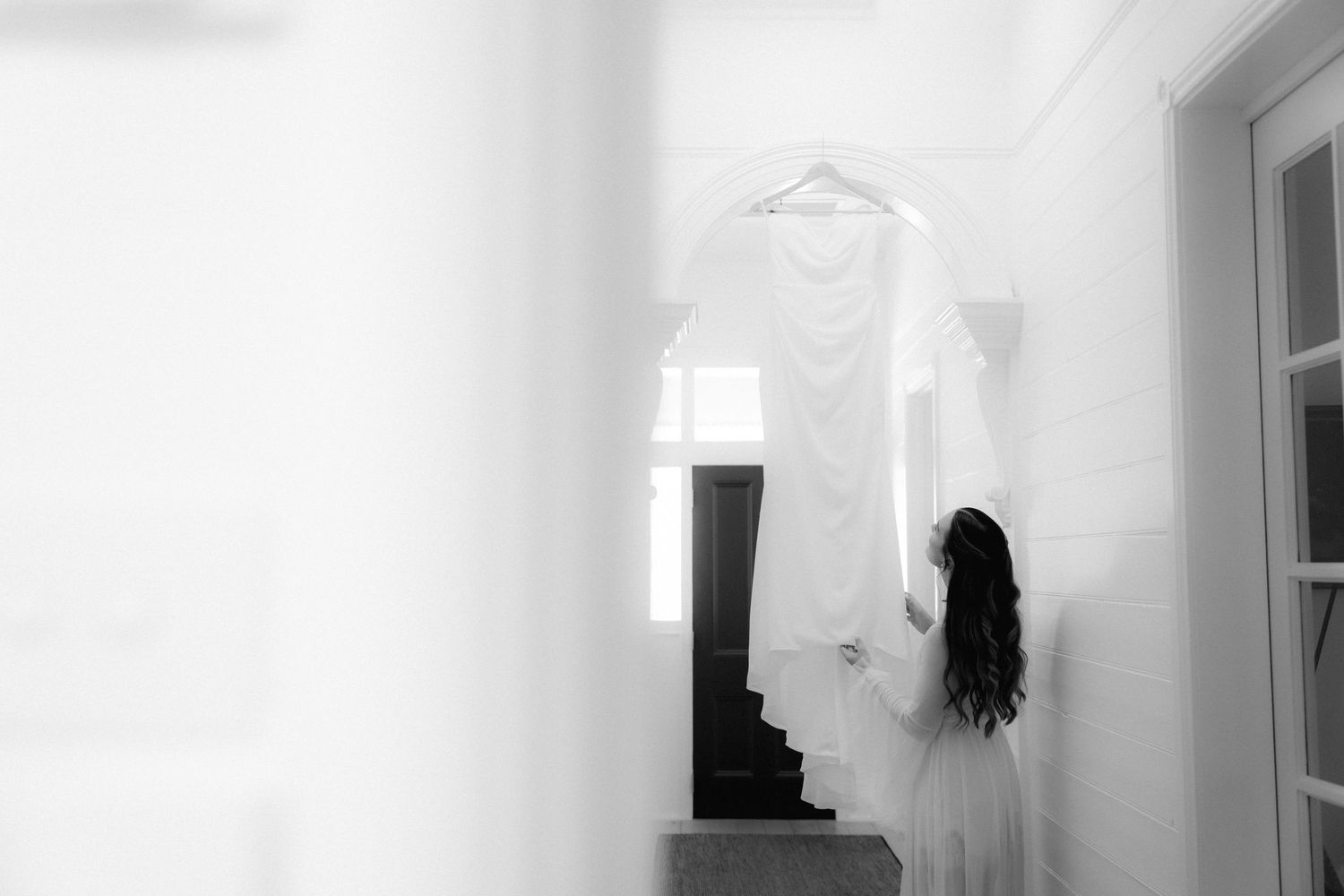 A white wedding dress hanging in a bright room with natural light coming through windows.