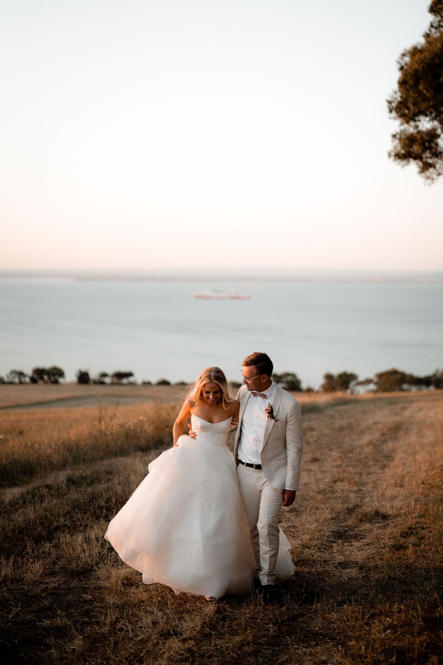 A romantic coastal wedding photoshoot in a golden field at sunset.