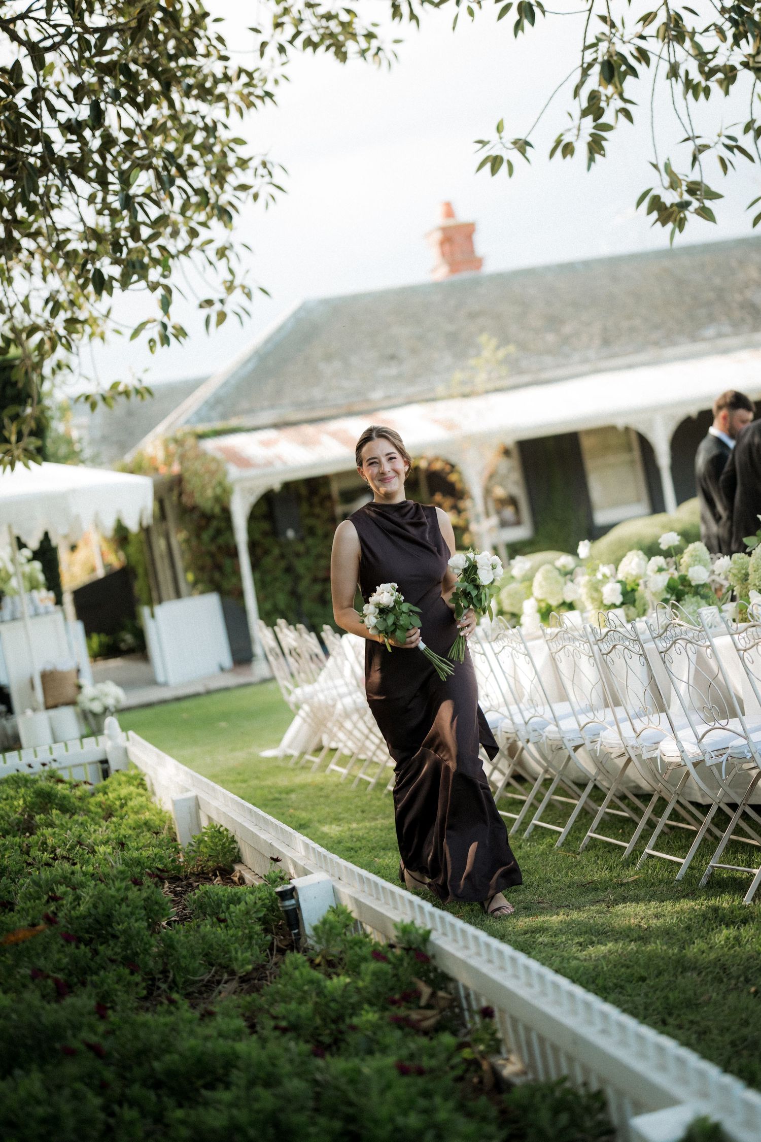 Wedding ceremony setup with white chairs and decorative elements in a garden setting.