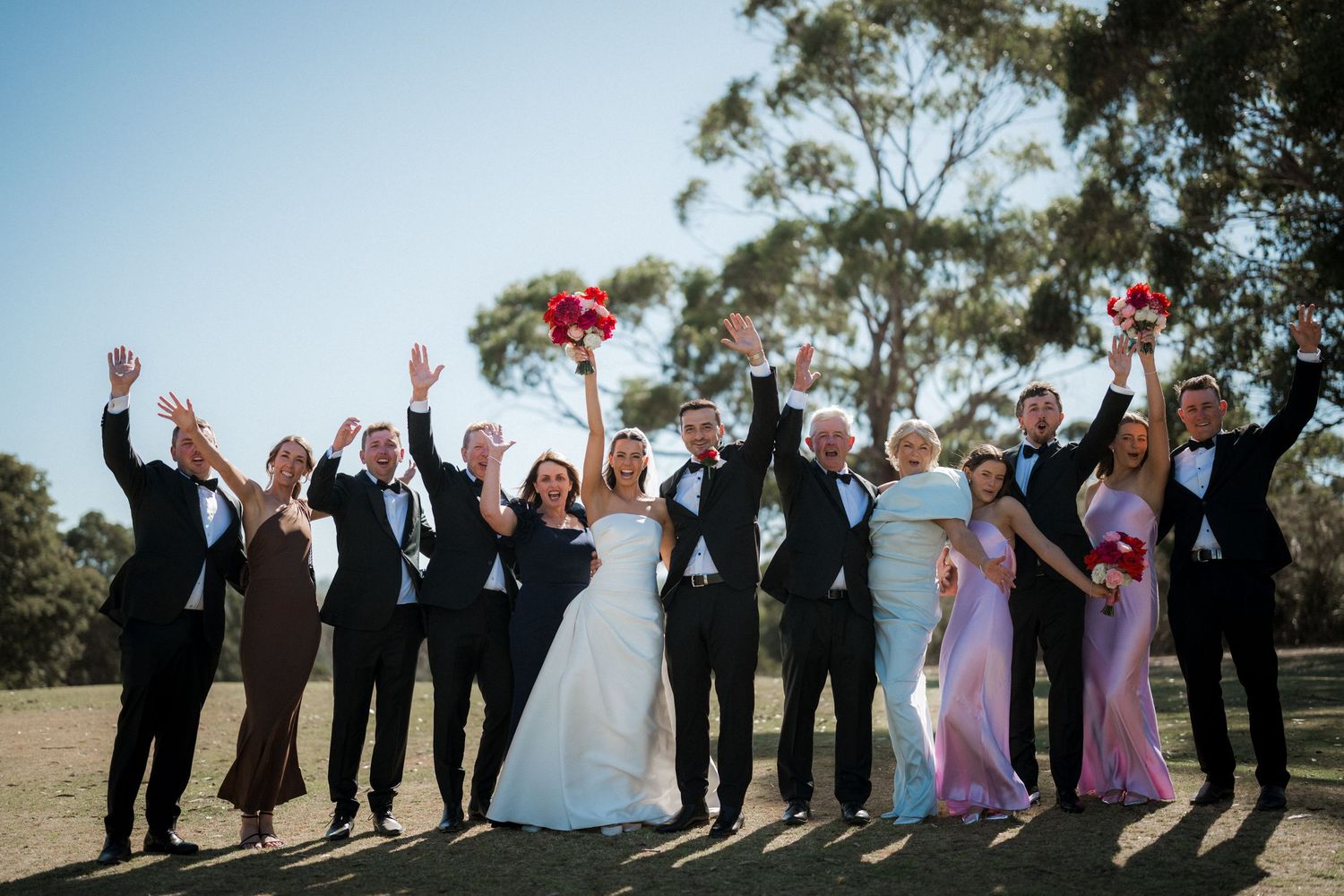 Wedding party lined up outdoors strikes fun poses while celebrating with joyful expressions.