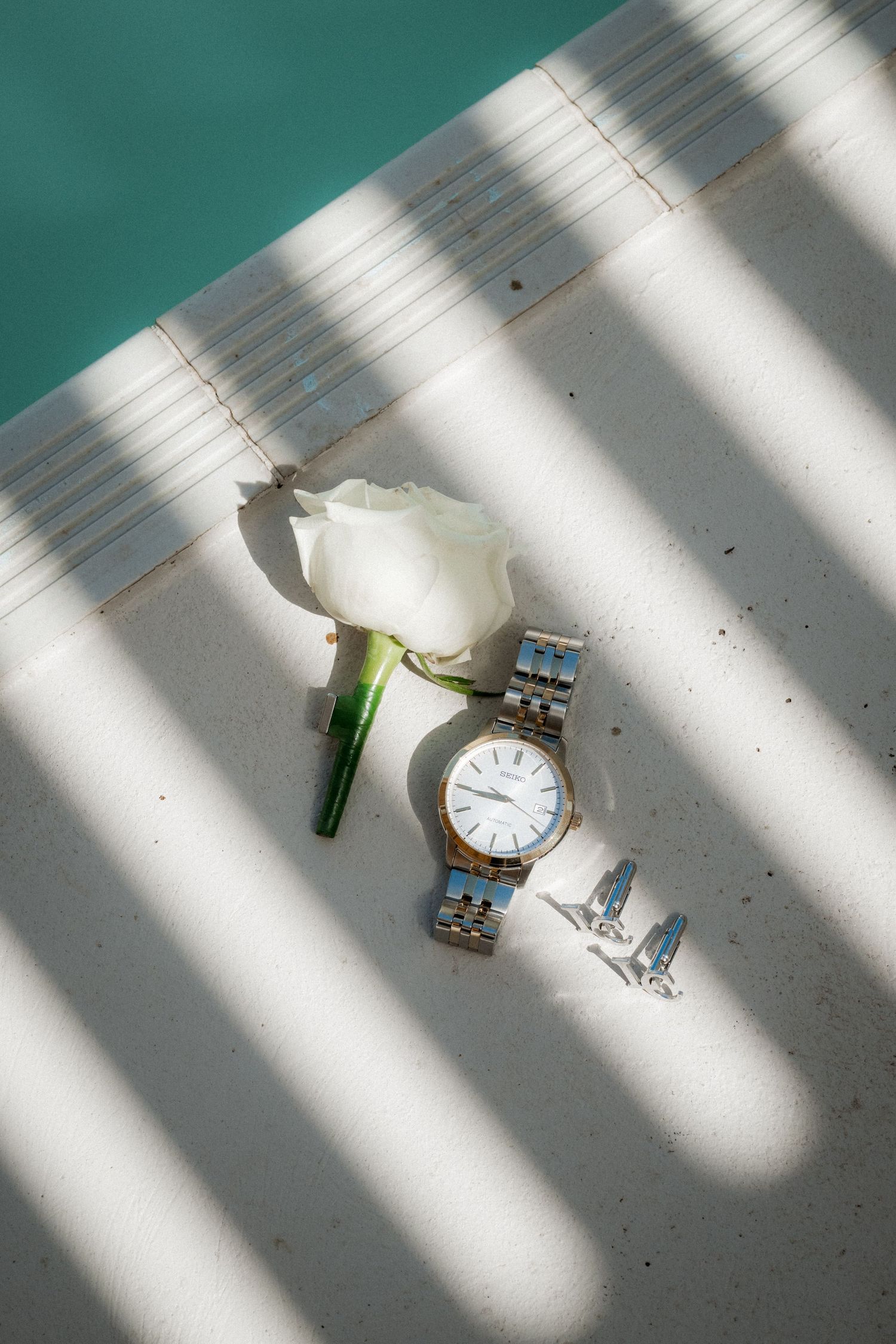Sunlight casts dramatic diagonal shadows across a white surface with an analog wristwatch in view.