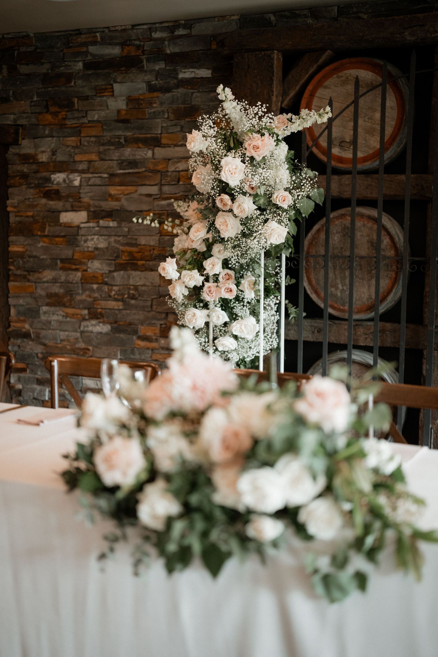 Romantic floral arrangements with pink and white blooms decorate a rustic wedding reception space.