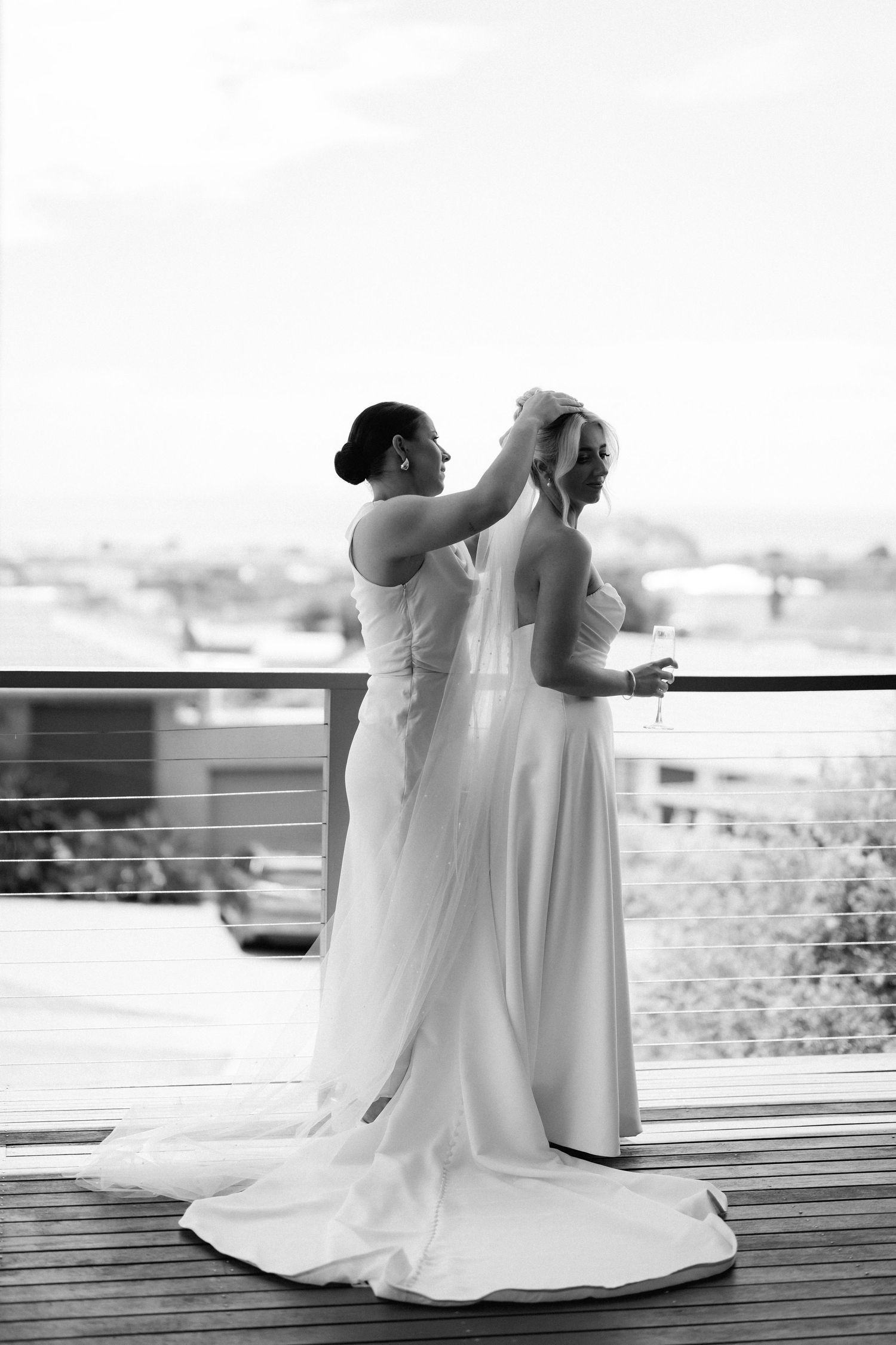 A black and white photo of final bridal preparations on a balcony overlooking a city.